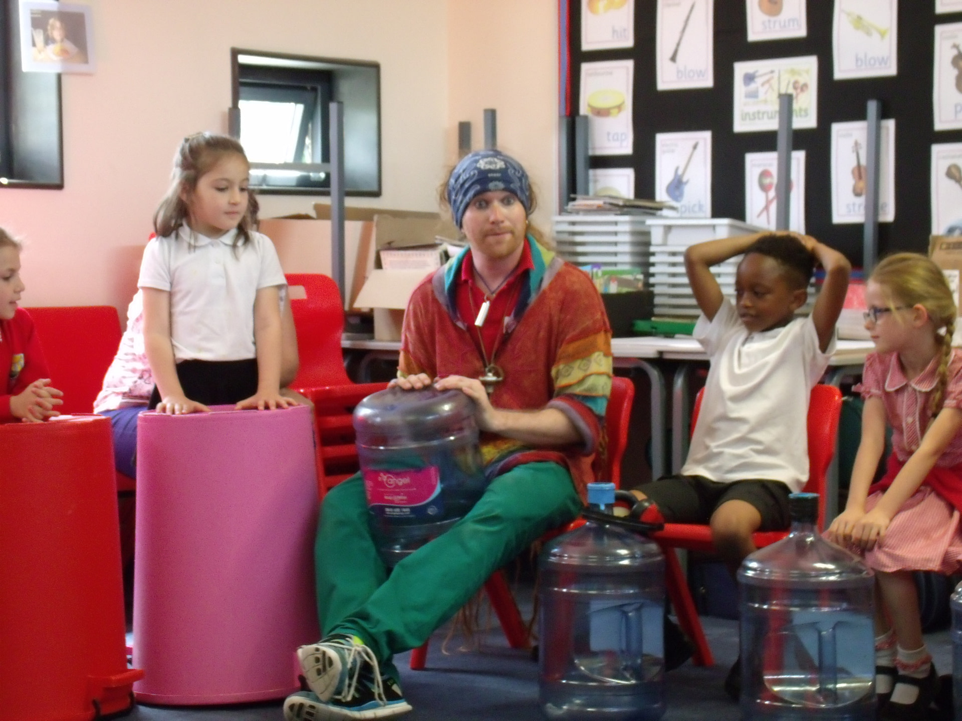School children and teacher playing music on large colourful empty bins and bottles