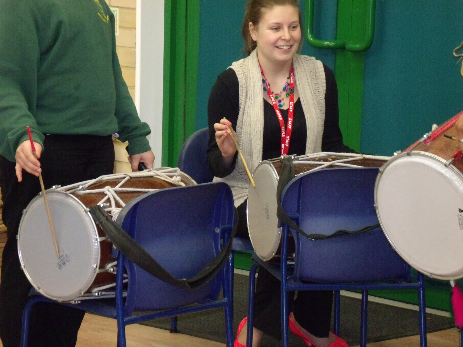 Teacher learning how to play indian drum in school hall on chair