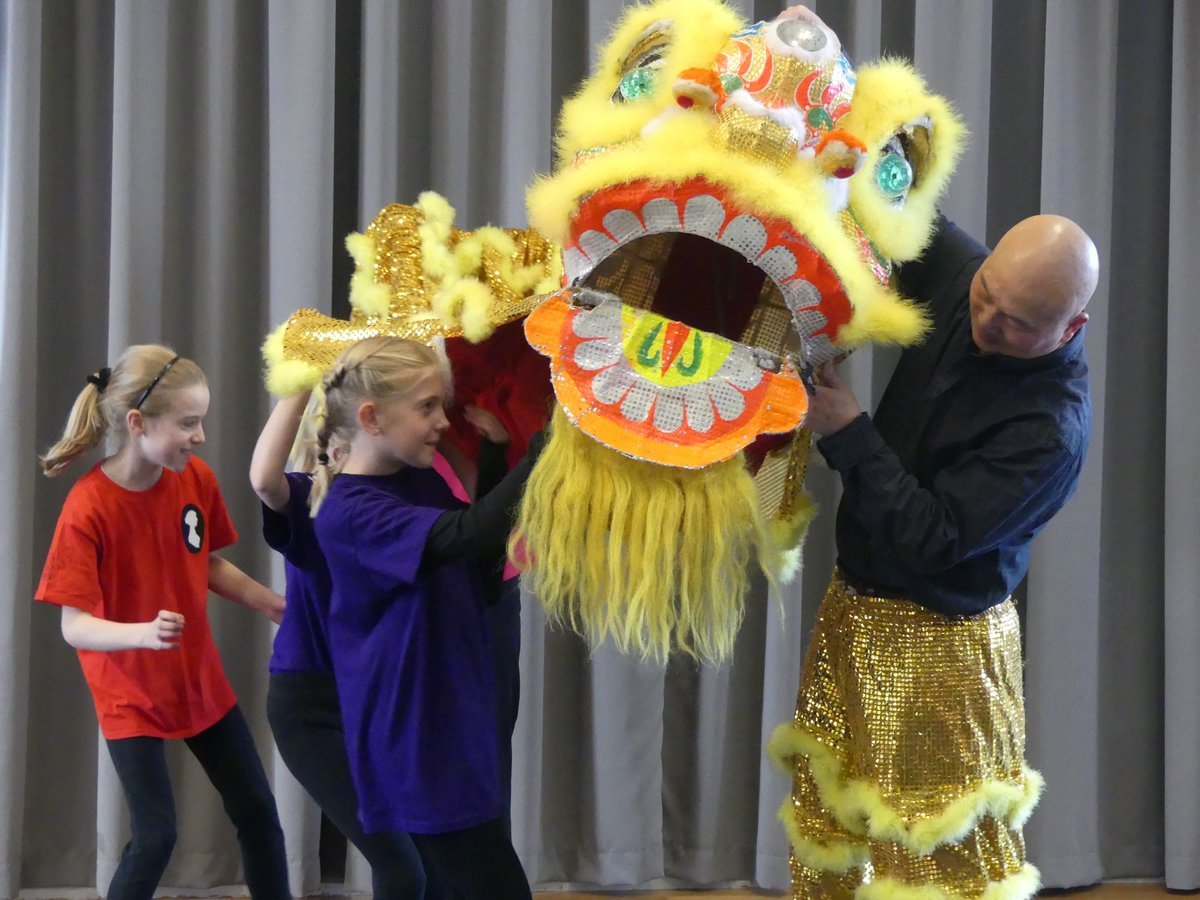 School children and teacher putting on yellow Chinese lion dance costume